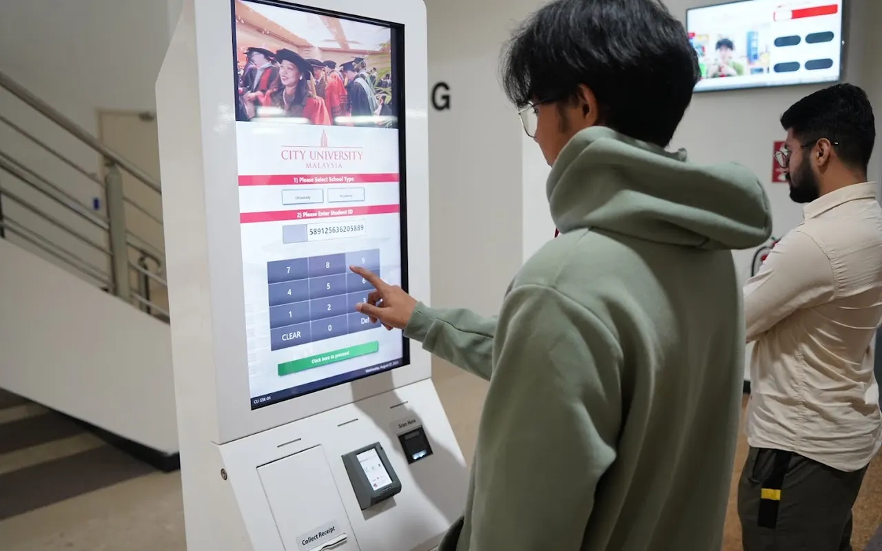 City University Malaysia kampusidagi axborot kioski yonida turgan talaba