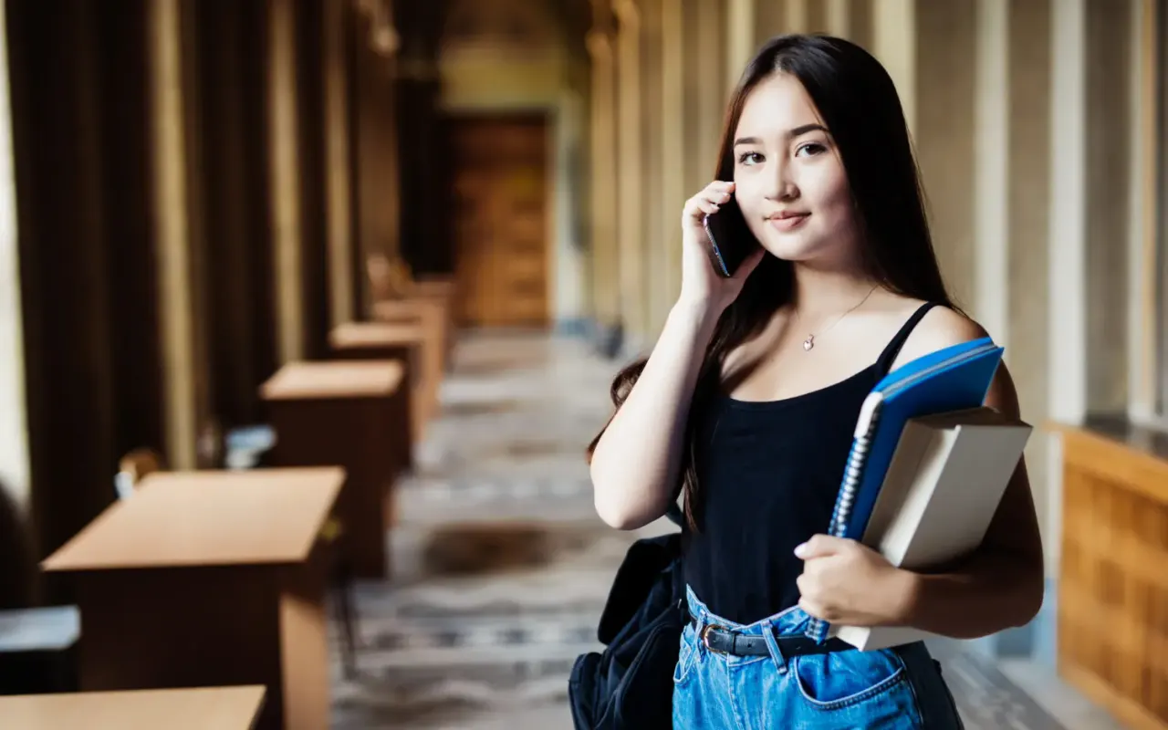 Darslik va telefon bilan xorijiy universitetga kirishga tayyorlanayotgan maktab bitiruvchisi